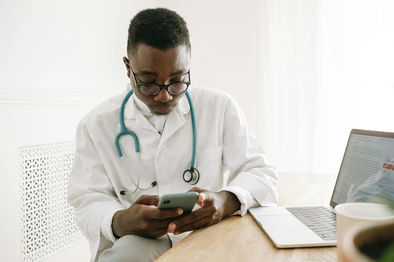 Image of a busy doctor posing with their laptop and googling on smartphone, symbolising someone who is concerned about compliance and regulations